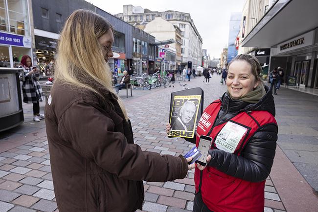 A Big Issue vendor taking a contactless payment from a customer