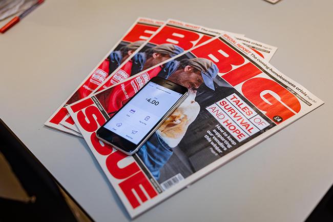 A phone displaying the cost of a copy of the Big Issue on top of three copies of the magazine