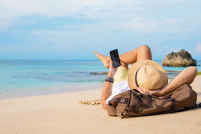 man laying on beach looking at phone
